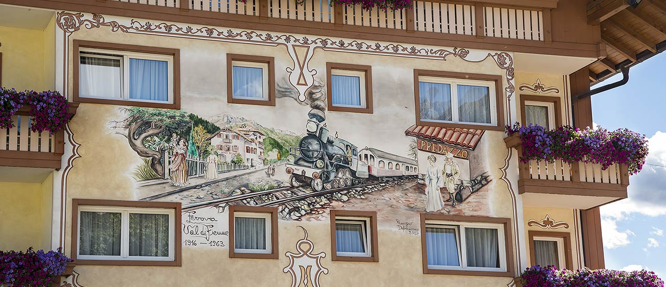 Una facciata di una casa del paese di Predazzo dipinta con un treno