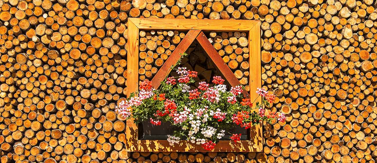 Parete fatta di ceppi di legno e gerani sul balcone