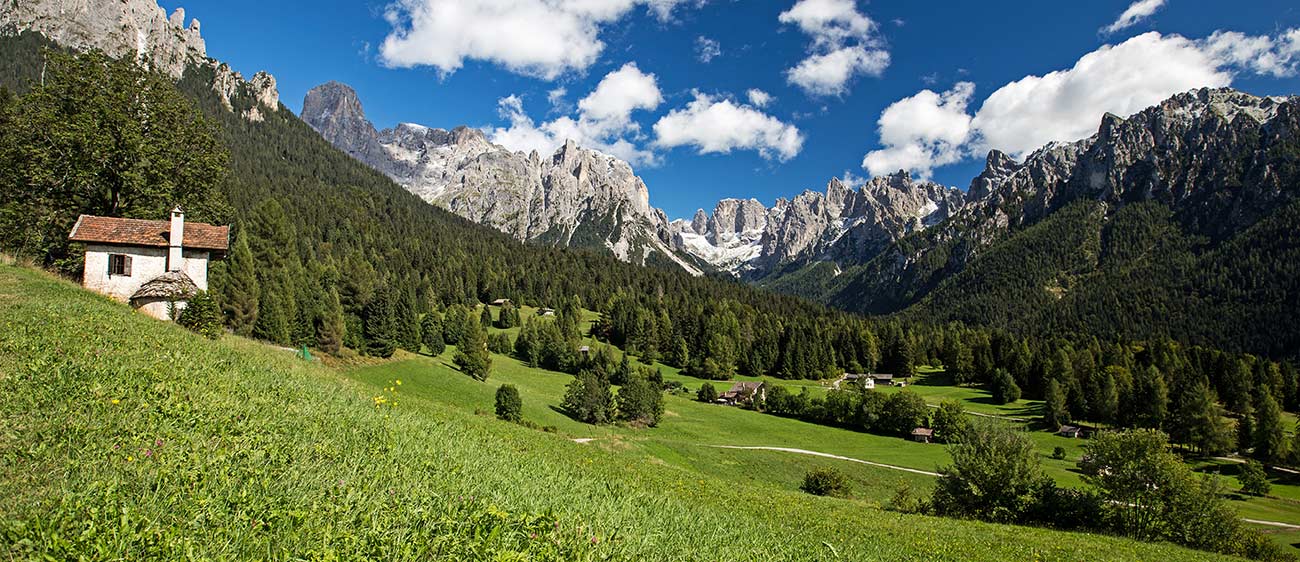 Una vista sulla Val di Fiemme con un'antica casetta, prati e boschi