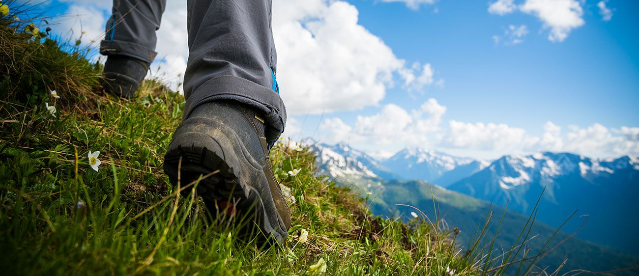 Details der Füße eines Wanderers, der einen grasbewachsenen Hang hinaufsteigt