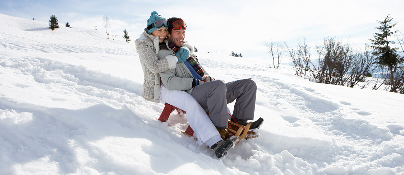 Frau umarmt ihren Mann während sie im Schnee mit einer Rodel fahren