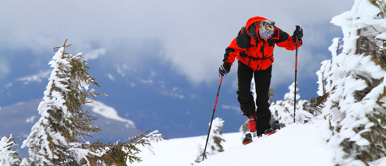 Persona con abiti rossi e neri fa sci alpinismo