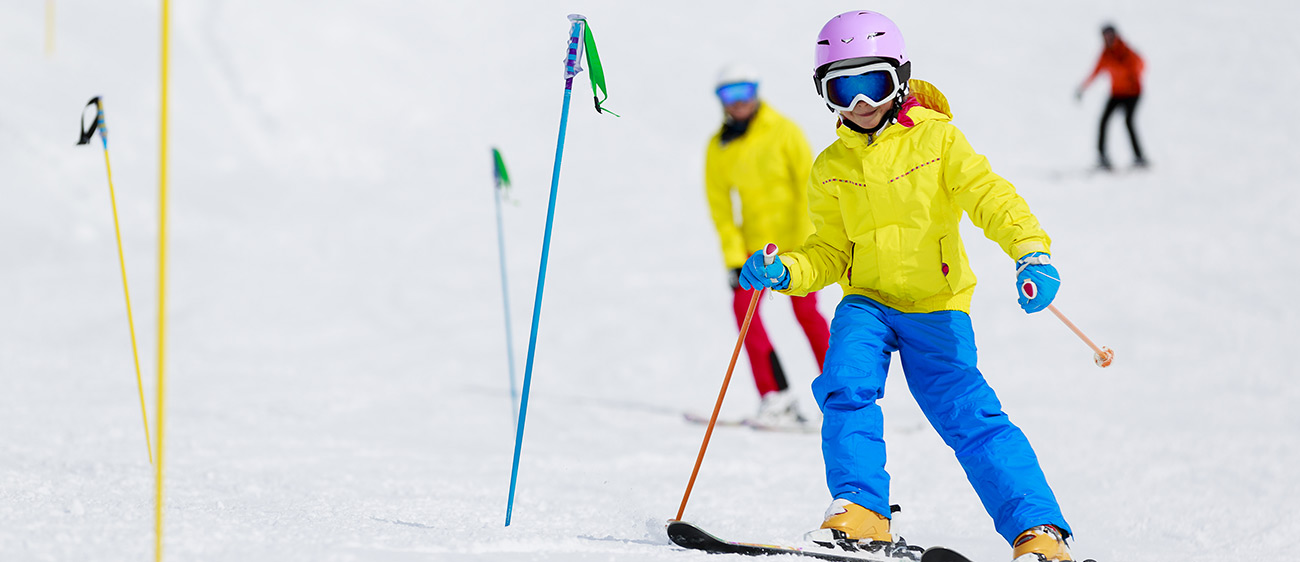 Bambina impara a sciare facendo slalom tra bacchette infilate nella neve