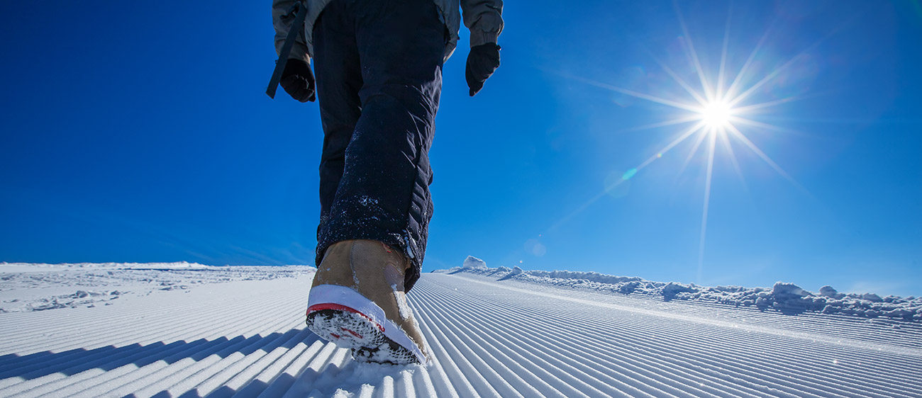 Person walking on snow with the sun shining in the sky