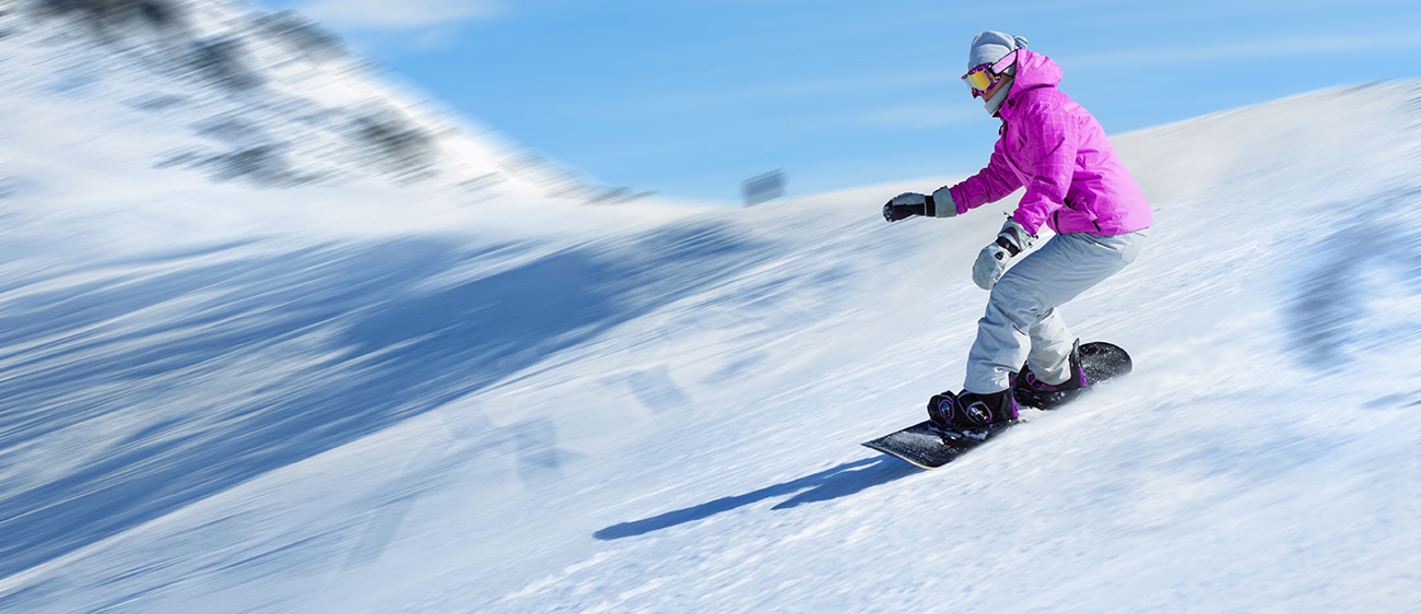 Snowboarderin mit rosa Jacke beim Runterfahren einer Piste in der Val di Fiemme