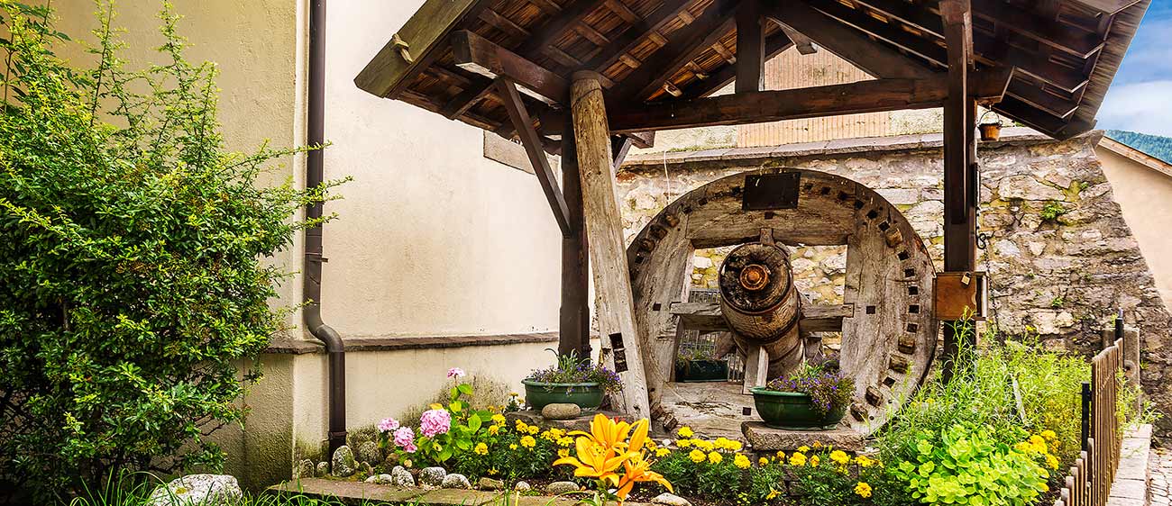 Das Rad einer alten hölzernen Wassermühle umgeben von Blumen
